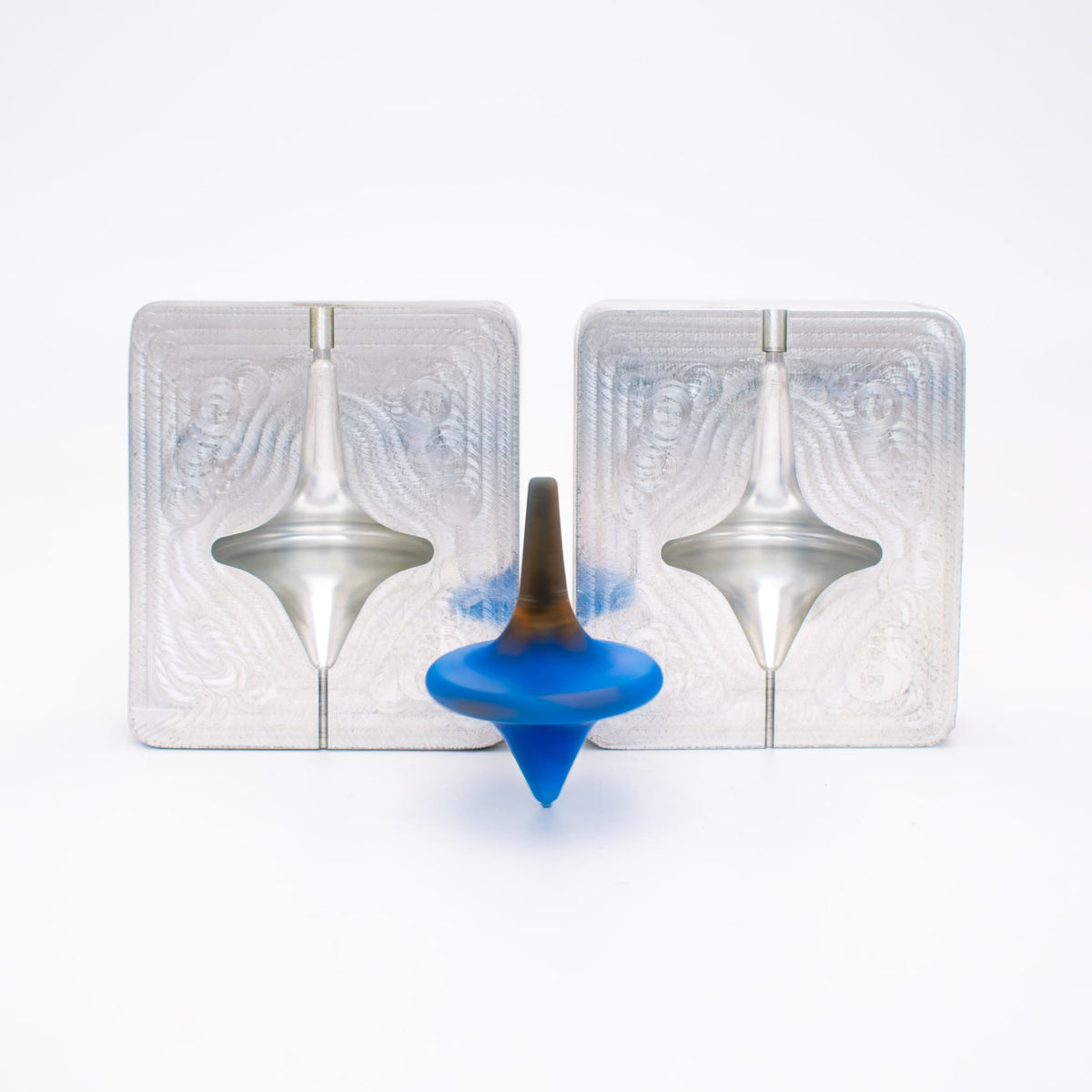 Two aluminum mold blanks machined into a two-part spinning top mold, with the TPE injection molded blue and brown top in front.