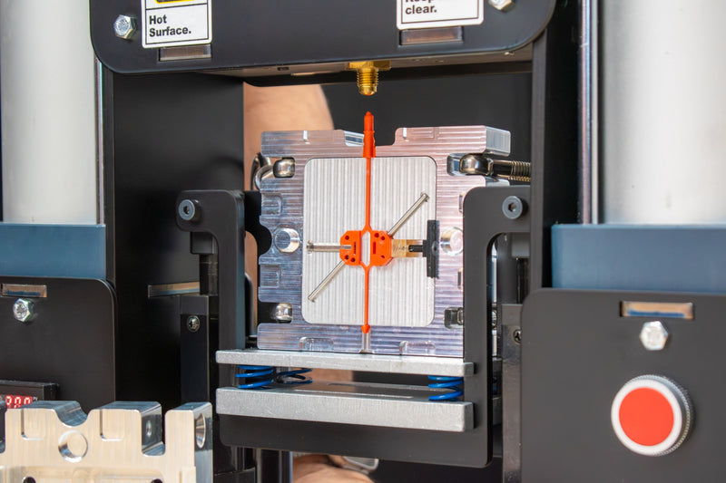 Plastic injected part inside an aluminum mold and mold backers by Action BOX sitting on the INJEKTO 3 desktop injection molding machine.