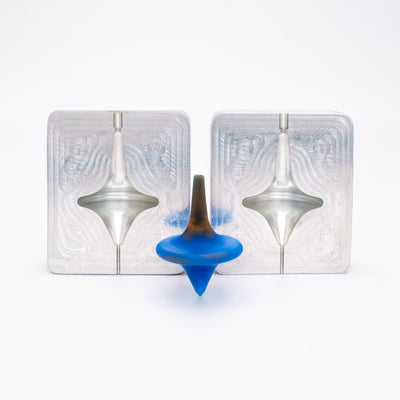 Two aluminum mold blanks machined into a two-part spinning top mold, with the TPE injection molded blue and brown top in front.